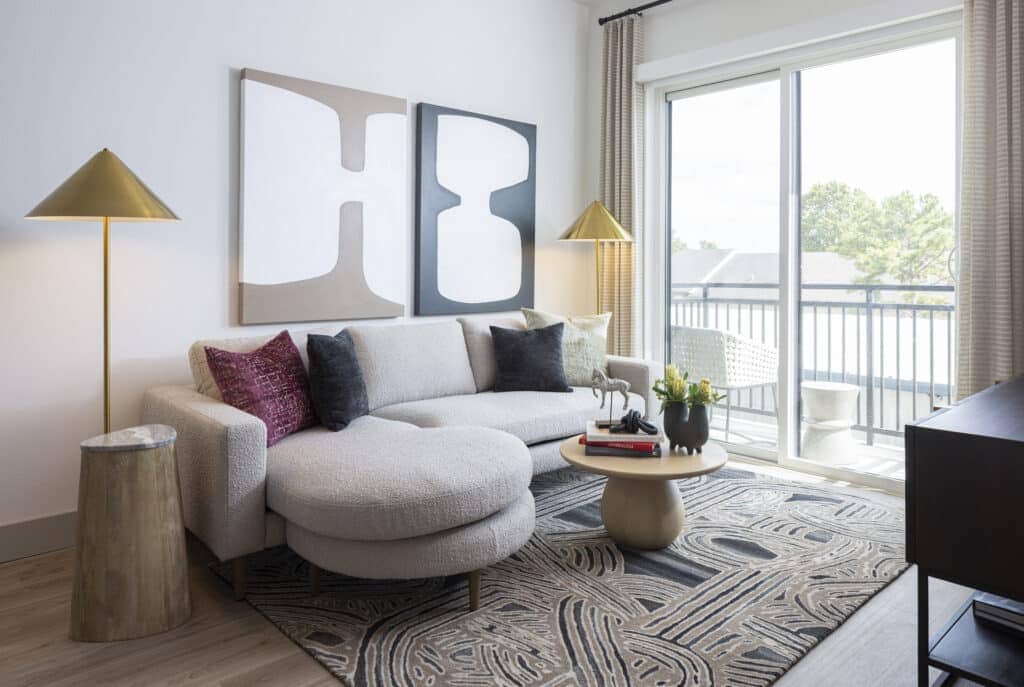 Living room with large painting behind white sofa with floor to ceiling windows at Broadstone Emeline Heights in Houston, TX